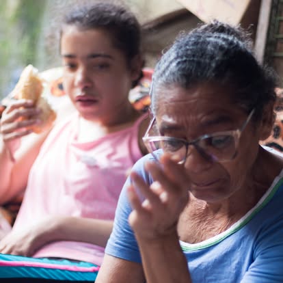 Auana comendo pão ao lado da avó